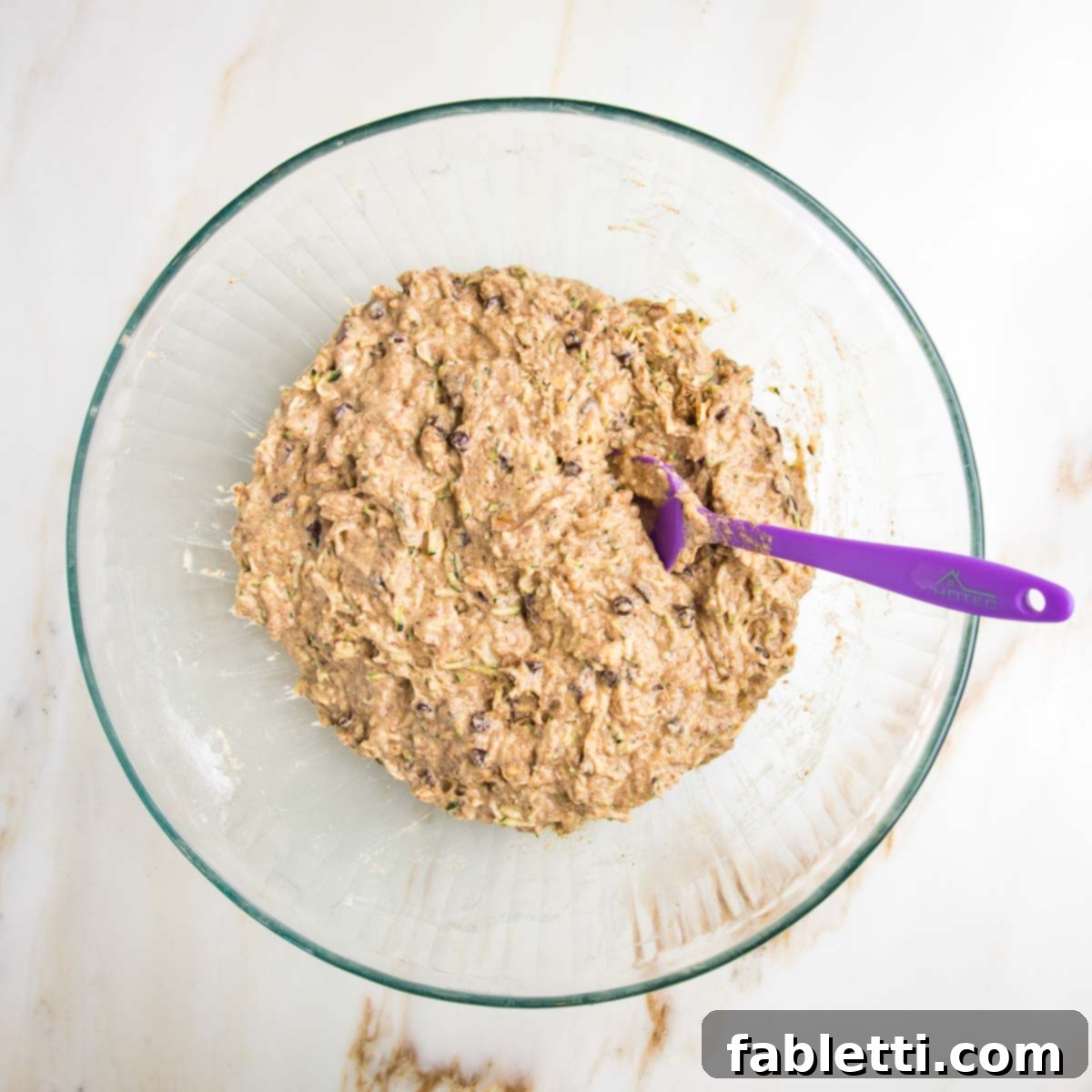 Garden Fresh Vegan Zucchini Muffins 12 Light brown zucchini muffin batter. You can see mini chocolate chips and the shredded zucchini and some chopped nuts.