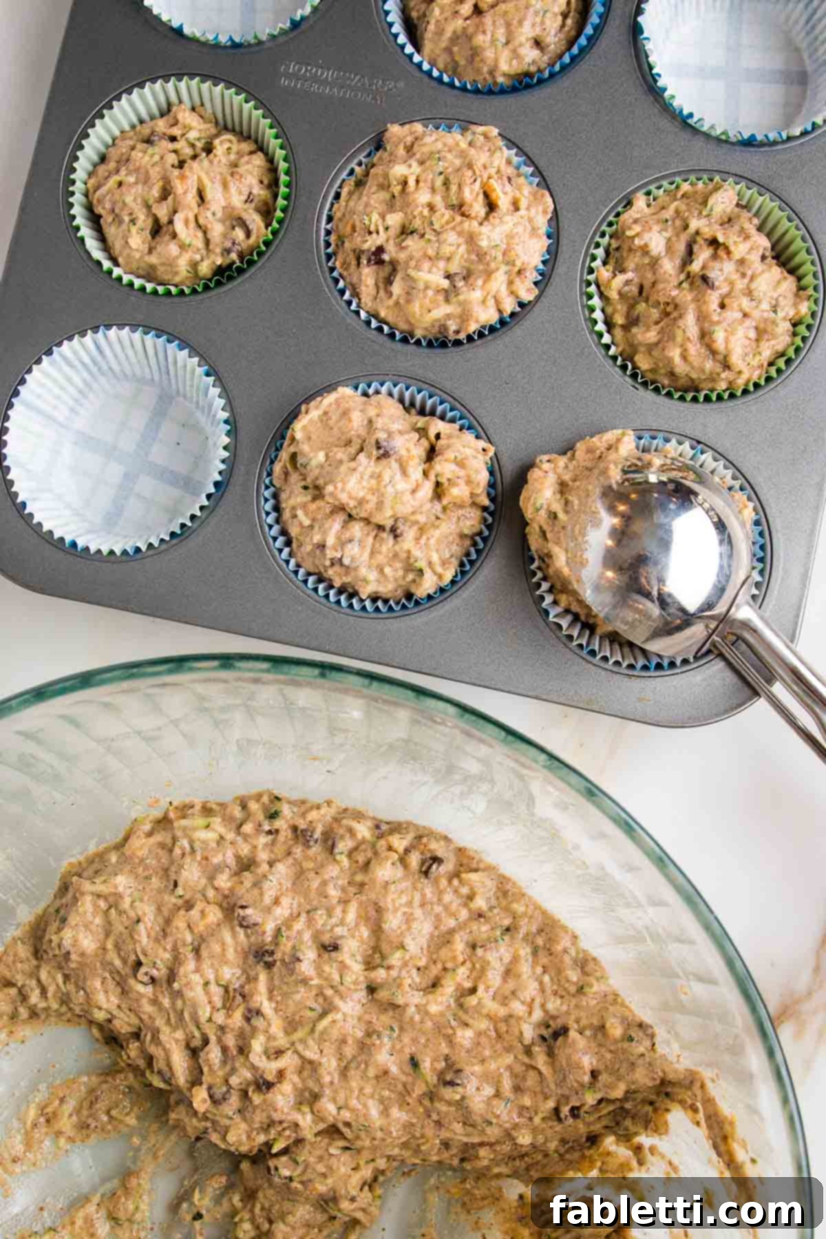 Garden Fresh Vegan Zucchini Muffins 13 Zucchini muffin batter in a large mixing bowl. Cookie scoop portioning batter into muffin tin lined with parchment paper liners.