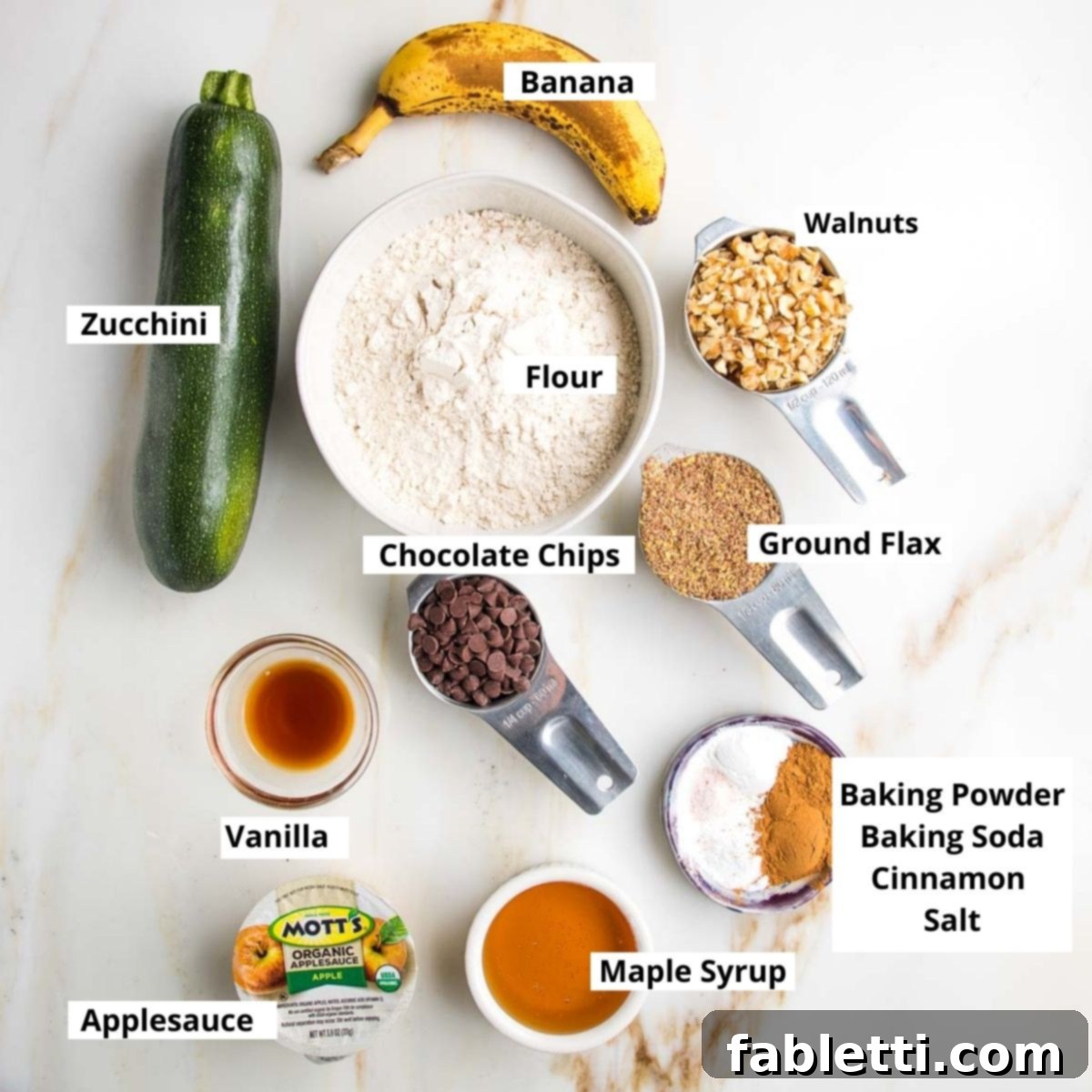 Garden Fresh Vegan Zucchini Muffins 3 Labeled zucchini muffin ingredients: banana, zucchini, flour, walnuts, flaxseed, chocolate chips, vanilla, maple syrup, baking soda, baking powder, cinnamon.