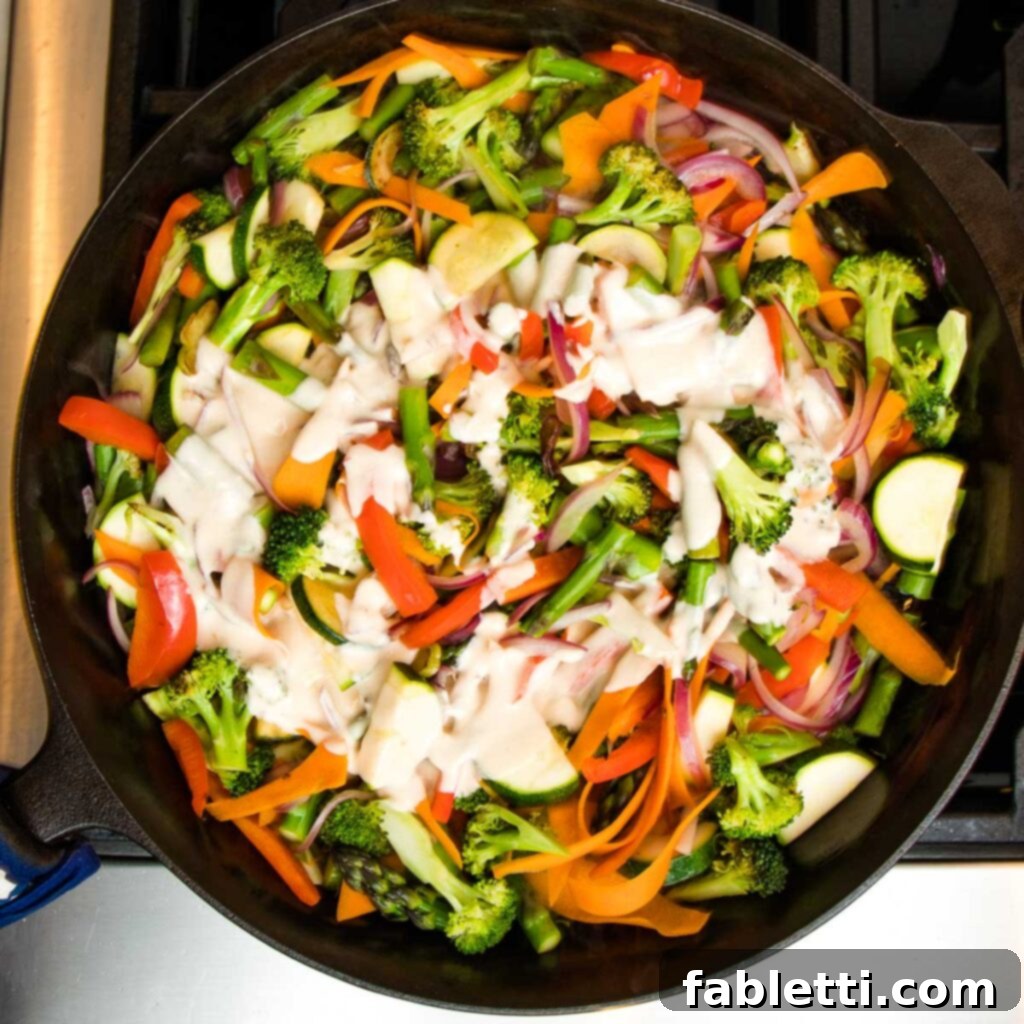 Vibrant Vegan Primavera Pasta 13 Cast iron skillet with colorful sauteed vegetables topped with a swirl of creamy primavera sauce.