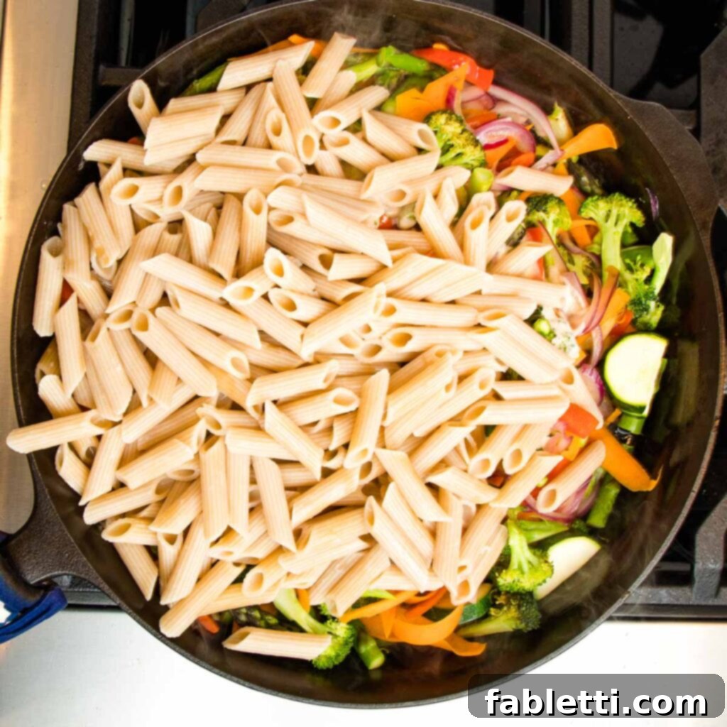 Vibrant Vegan Primavera Pasta 14 Cast iron skillet filled with colorful sauteed vegetables and topped with just cooked penne pasta.