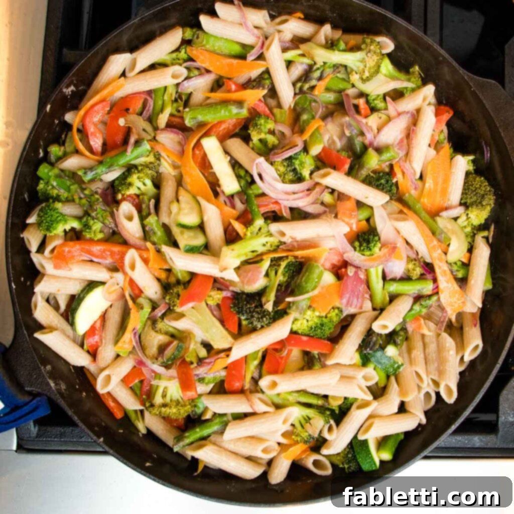 Vibrant Vegan Primavera Pasta 15 Cooked penne pasta carefully transferred onto the bed of vibrant sautéed vegetables in a large skillet.