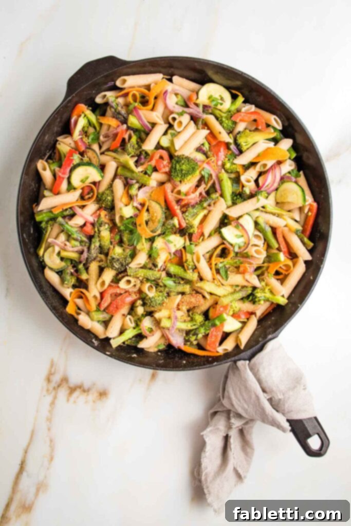 Vibrant Vegan Primavera Pasta 16 Cast iron skillet, with linen napkin on handle, filled with colorful veggies and pasta.