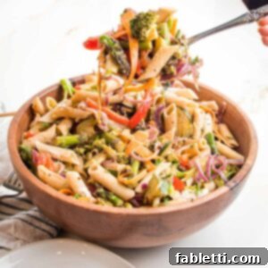 Vibrant Vegan Primavera Pasta 20 wooden bowl filled with penne pasta and lots of colorful veggies. There is a large spoon scooping up a bunch to plate.