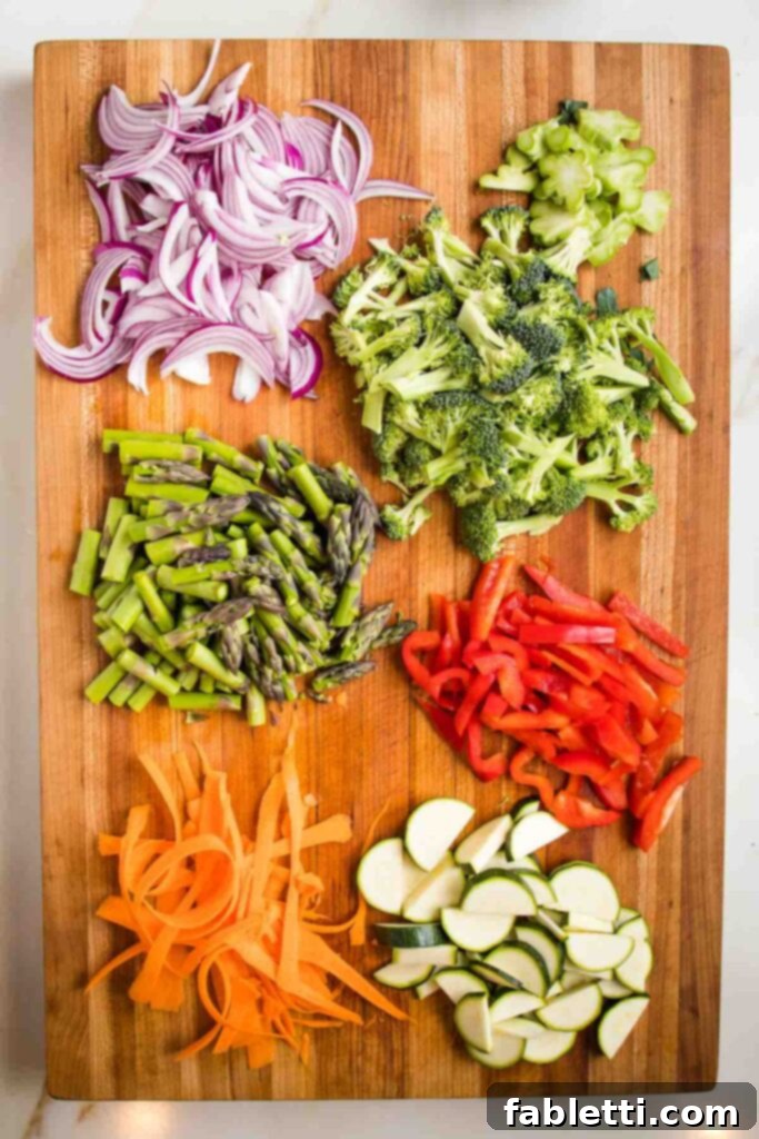 Vibrant Vegan Primavera Pasta 5 Wooden board with sliced red onion, broccoli florets, asparagus, red bell pepper, carrots and zucchini half moons.