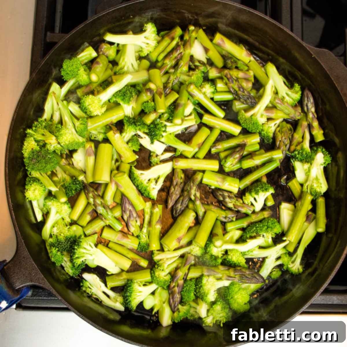 Vibrant Vegan Primavera Pasta 7 Close-up of chopped broccoli stalks, asparagus spears, and florets being added to a hot skillet.