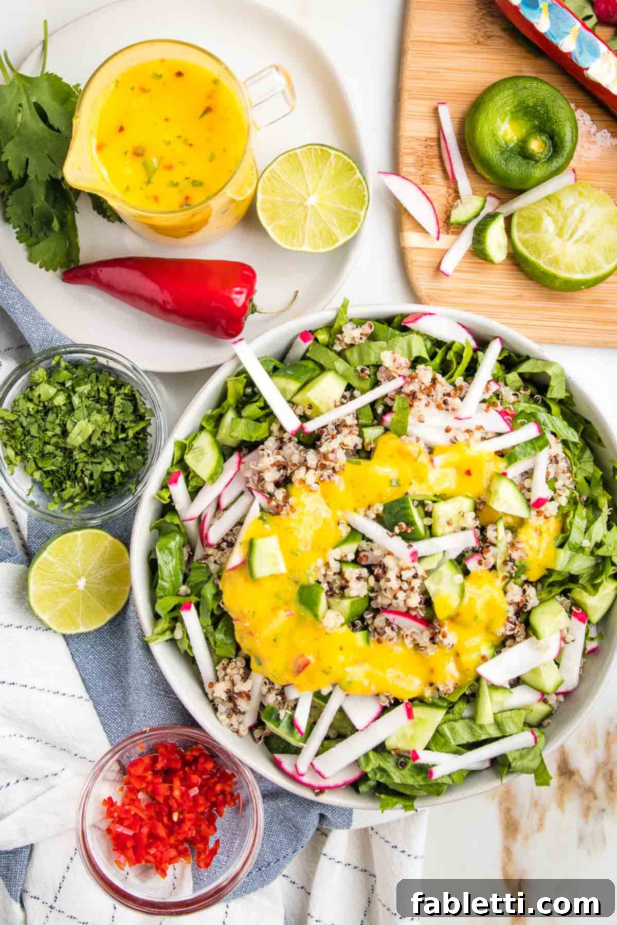 Tropical Mango Vinaigrette 2 Bright yellow mango salad dressing in a glass pitcher, a bowl of simple salad with same yellow dressing, lots of colorful chopped veggies strewn about.