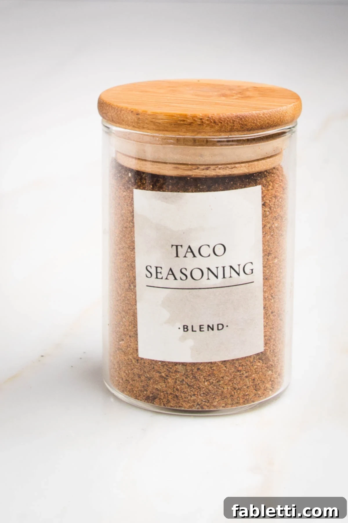 Salt-Free Homemade Taco Seasoning 2 Small spice jar with wooden lid labeled "taco seasoning-blend" with a orangy-rust colored powder inside.