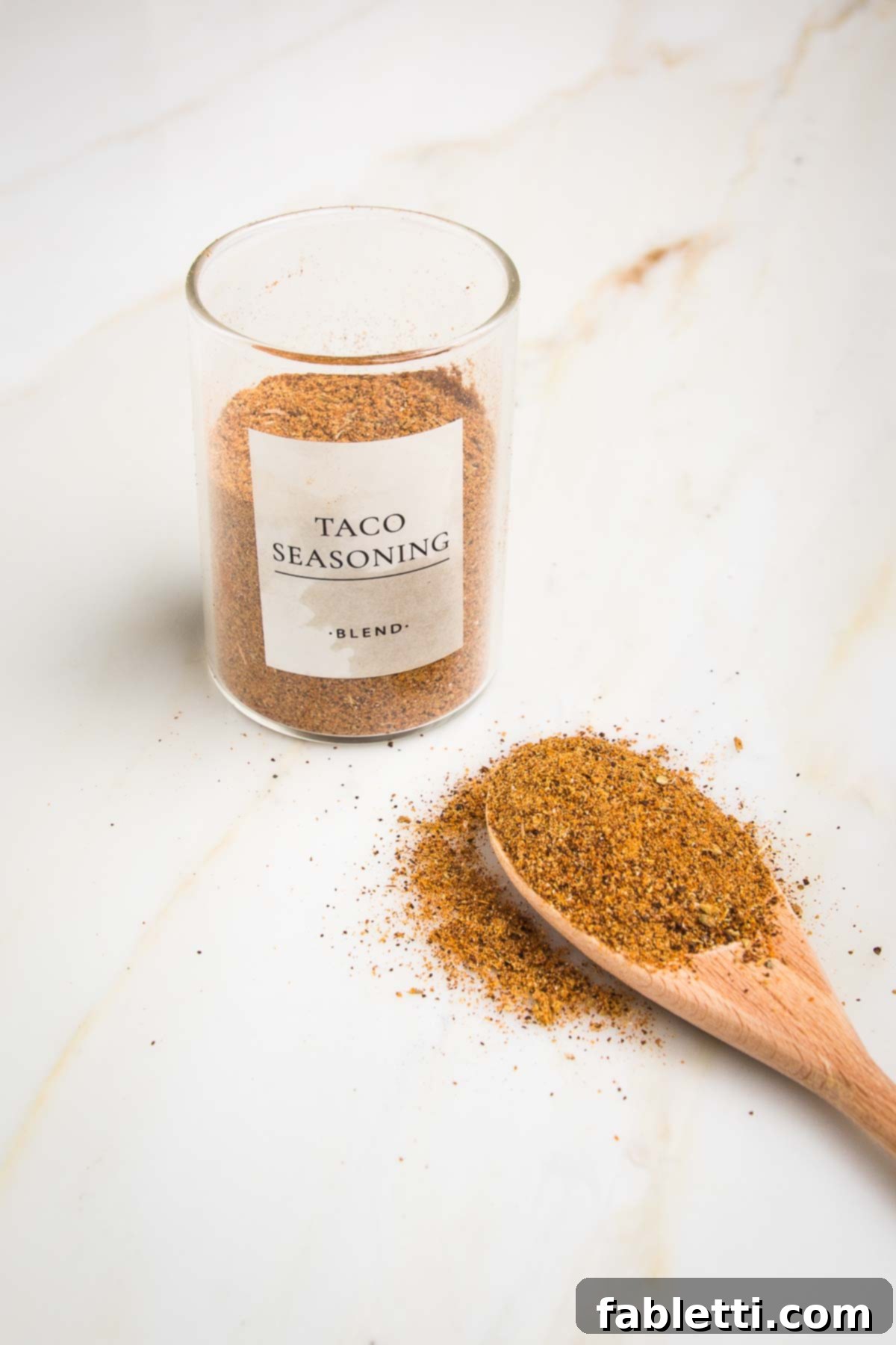 Salt-Free Homemade Taco Seasoning 3 Small glass jar labeled Taco Seasoning Blend ¾ filled with orangish brown powder and a wooden spoon in front of it with same seasoning.