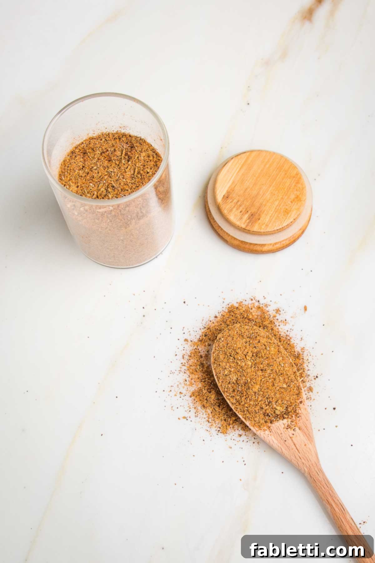 Salt-Free Homemade Taco Seasoning 5 Small jar with taco seasoning blend, wooden top off to the side. Wooden spoon filled with seasoning and some around the spoon on the counter.