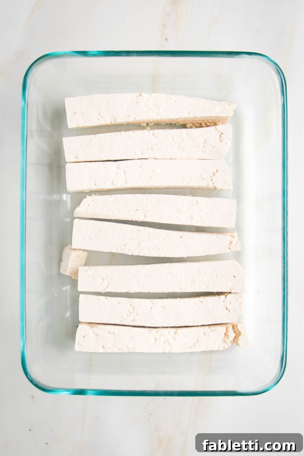 Grilled Tofu Satay with Creamy Peanut Sauce 12 Long, thin slices of tofu for satay in a rectangular glass dish.