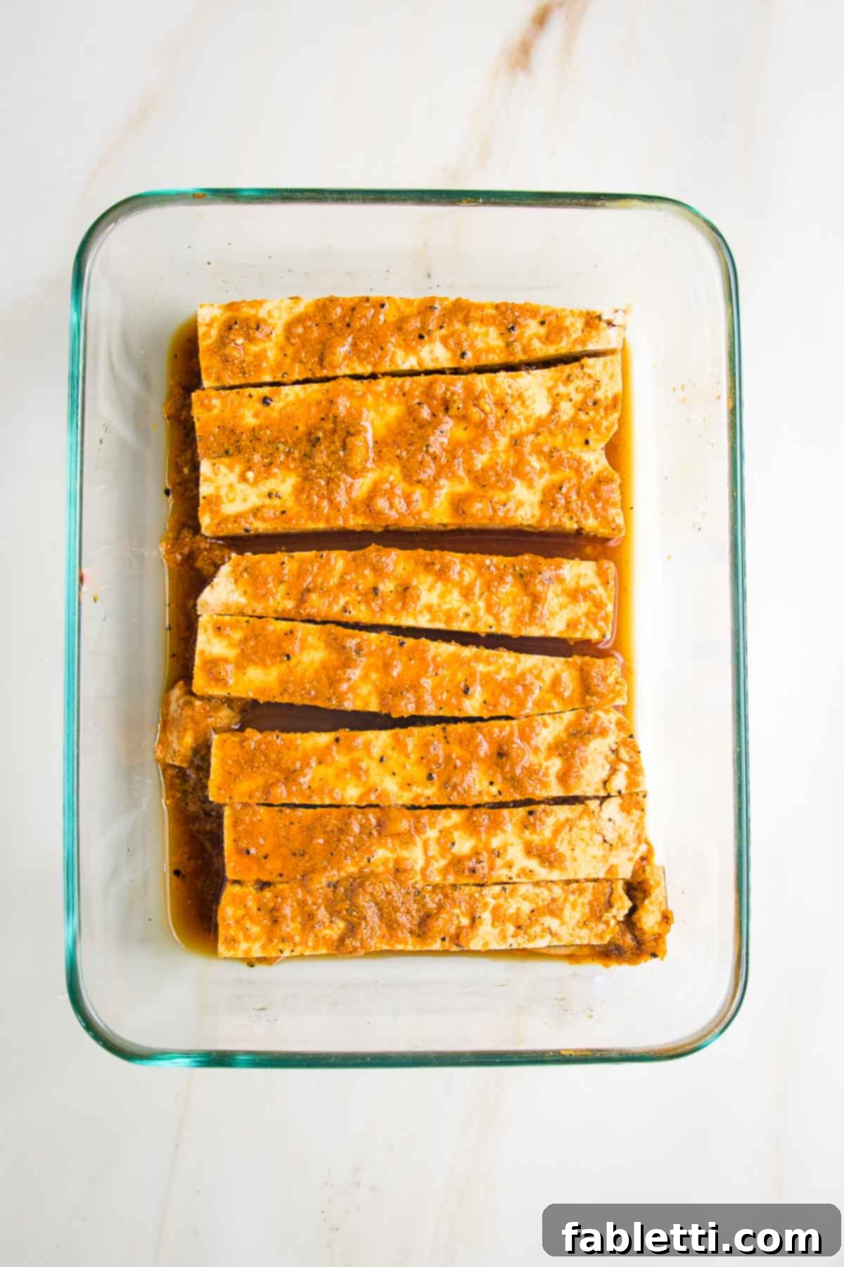 Grilled Tofu Satay with Creamy Peanut Sauce 13 Long thin slices of tofu for satay with brownish-orange marinade in a rectangular glass dish.