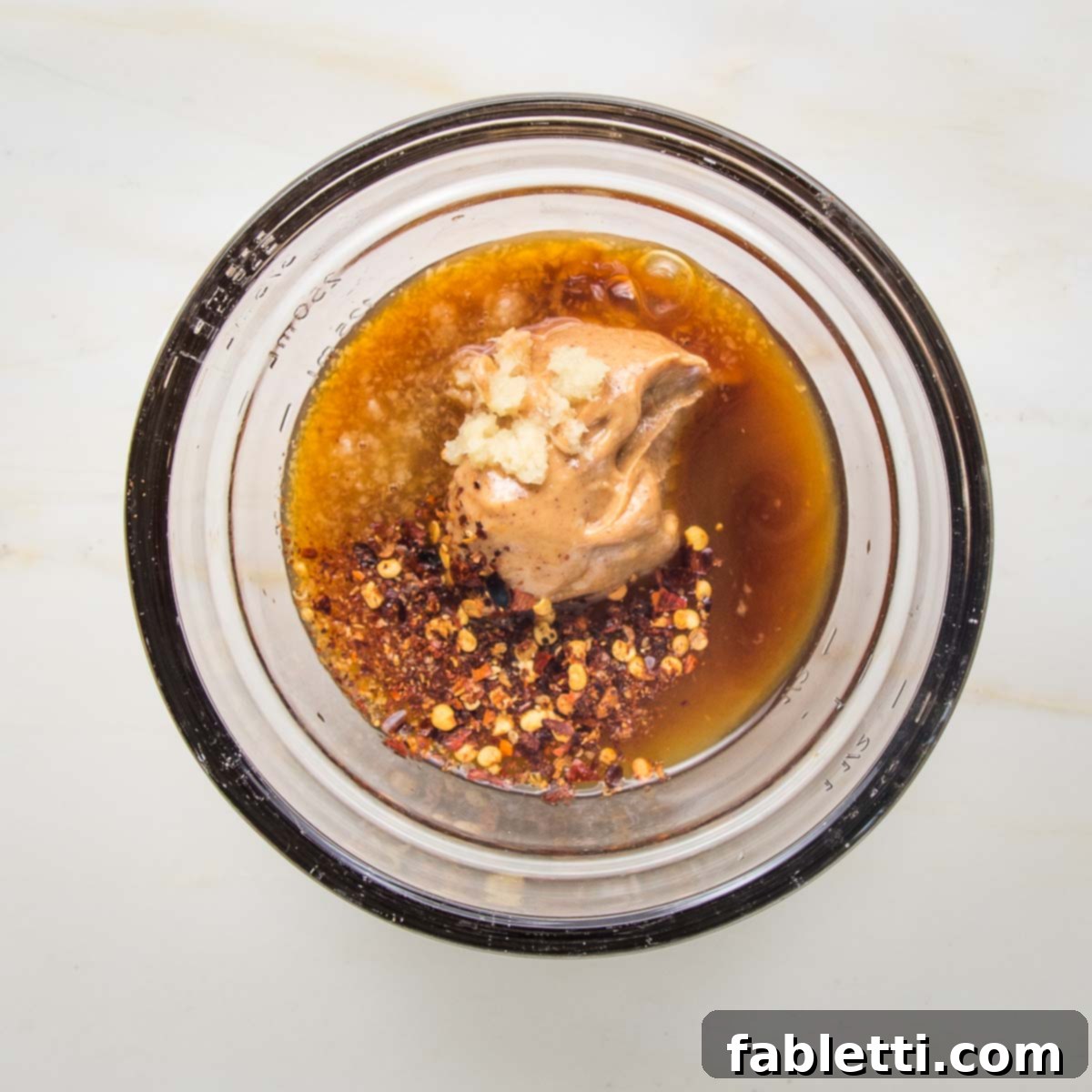 Grilled Tofu Satay with Creamy Peanut Sauce 8 Small glass bowl with peanut butter, tamari, other liquid and some crushed red pepper visible.