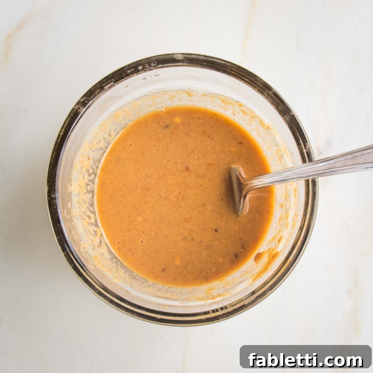 Grilled Tofu Satay with Creamy Peanut Sauce 9 Small glass bowl with fork that's mixed together an orangy-brown peanut butter sauce.