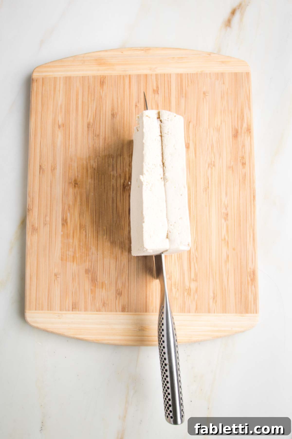 Grilled Tofu Satay with Creamy Peanut Sauce 10 Slicing through a block of tofu, on a wooden cutting board.