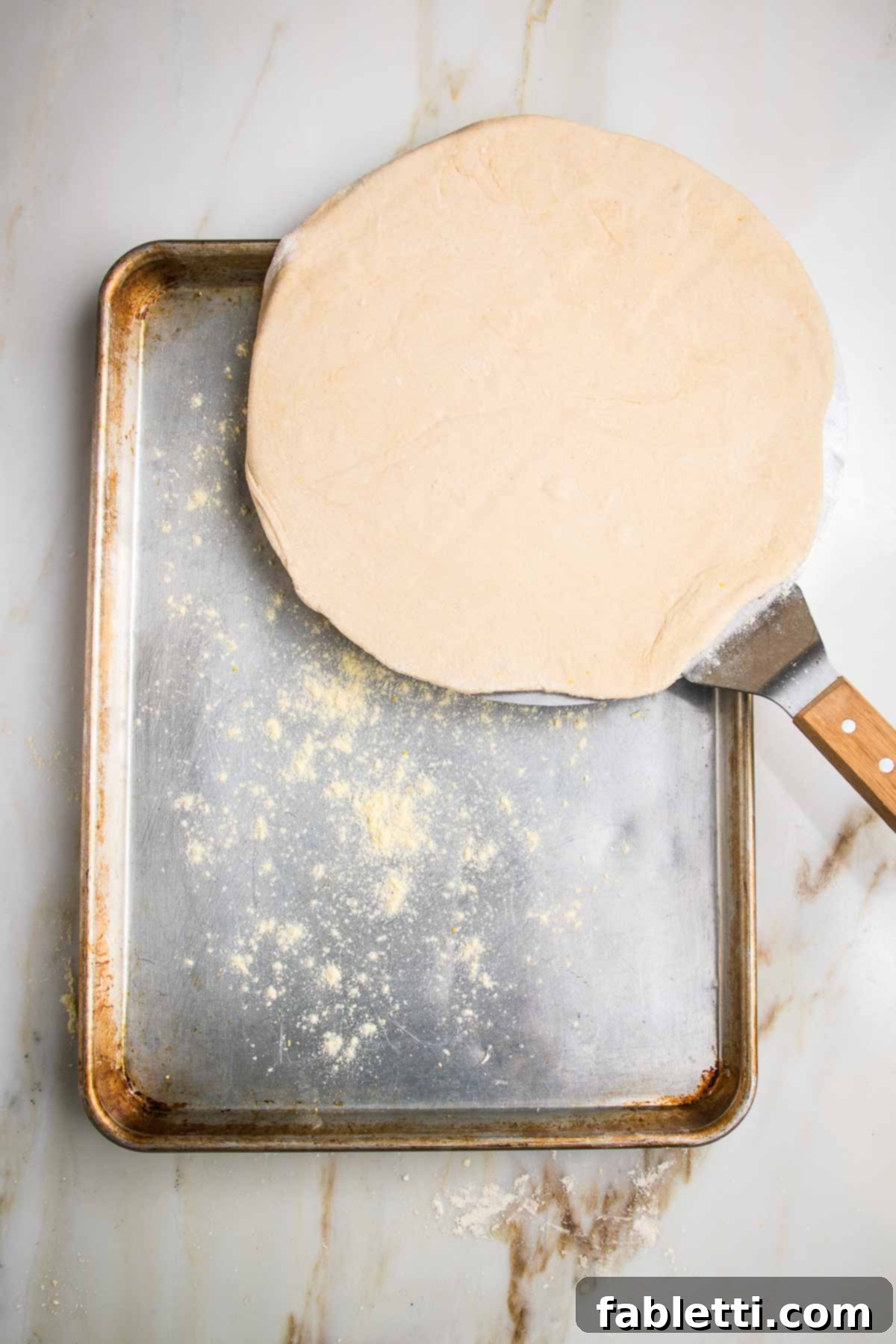Effortless Yeast-Free Flatbread Pizza 12 A heavy baking sheet, lightly sprinkled with cornmeal, positioned next to a rolled out flatbread dough on a pizza peel, ready for baking.