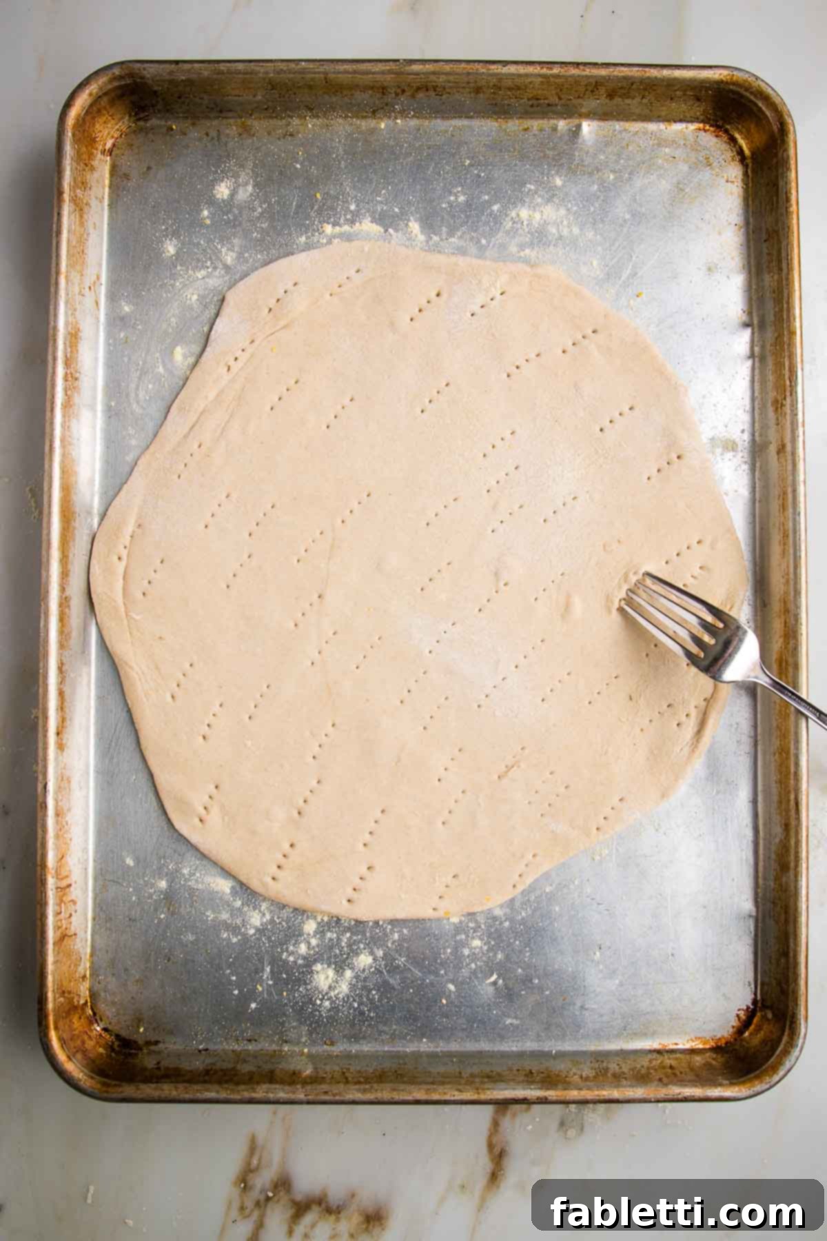 Effortless Yeast-Free Flatbread Pizza 13 Flatbread pizza dough, rolled out and placed on a baking sheet, with a fork actively pricking holes across its surface.