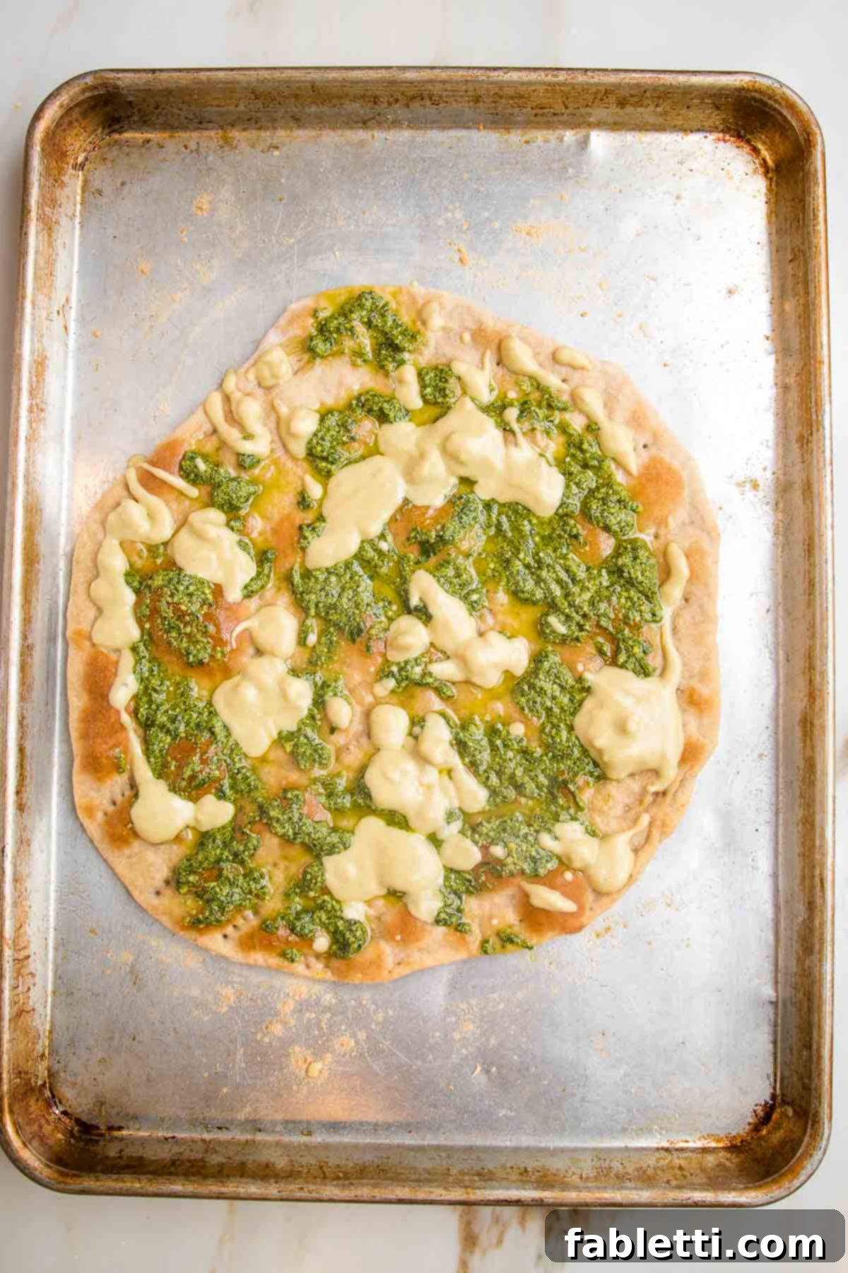 Effortless Yeast-Free Flatbread Pizza 15 Flatbread pizza dough freshly baked, with dollops of vibrant hummus and pesto spread on top, forming a flavorful base for additional toppings.
