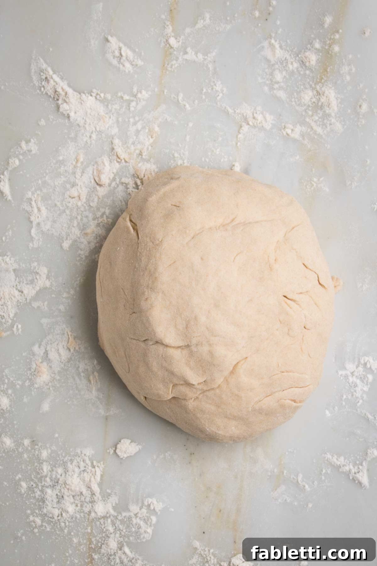 Effortless Yeast-Free Flatbread Pizza 8 A large, perfectly formed ball of no yeast flatbread dough resting on a floured marble counter, ready for division and rolling.