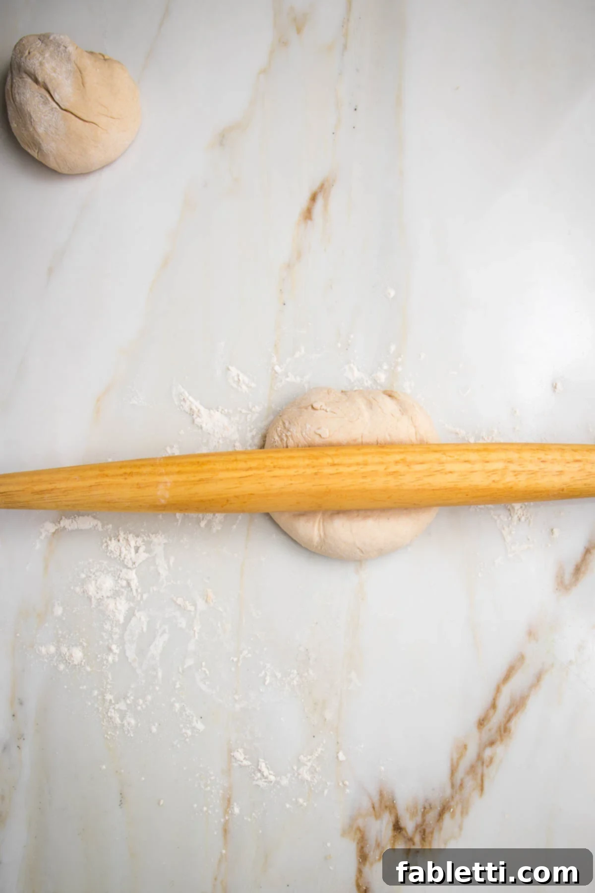 Effortless Yeast-Free Flatbread Pizza 9 No yeast flatbread dough, split into two pieces. A wooden rolling pin is actively rolling out one half of the dough into a thin shape.