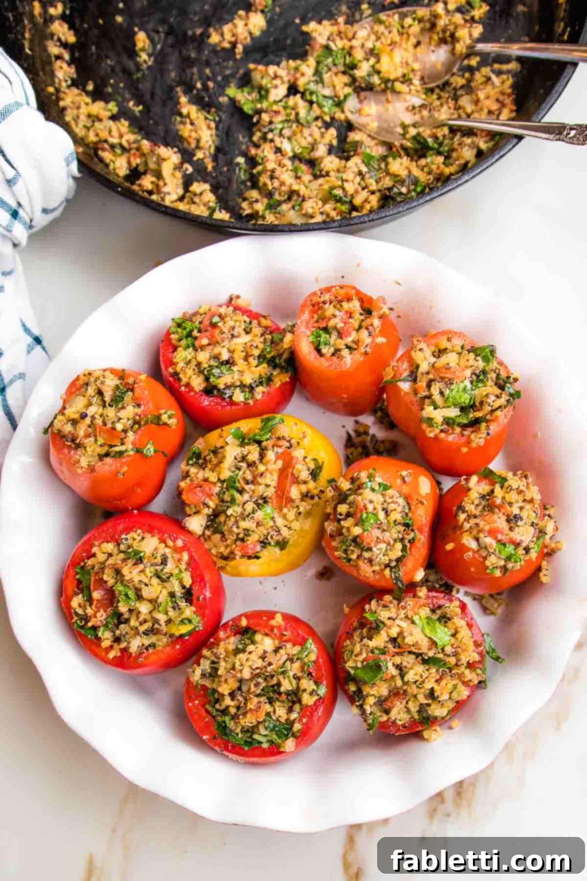 Plant-Powered Stuffed Tomatoes 14 Baking dish with scooped-out tomatoes, meticulously filled with the quinoa stuffing. A cast iron skillet with the remaining stuffing is visible in the background.