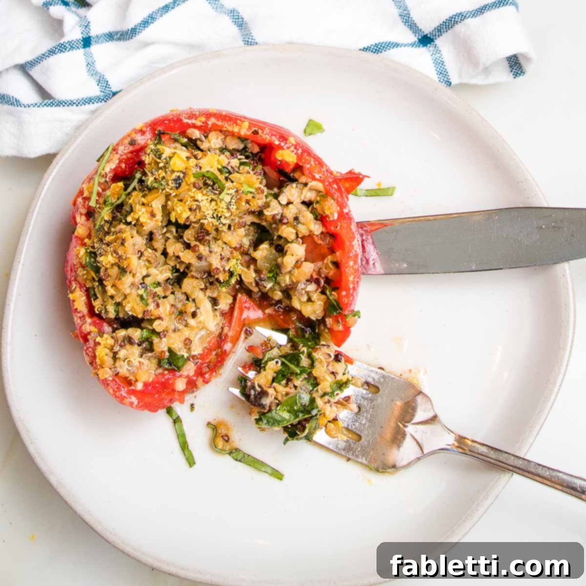 Plant-Powered Stuffed Tomatoes 16 A single baked stuffed tomato with quinoa, vegetables, and greens on a plate, with a bite on a fork, highlighting its delicious texture.