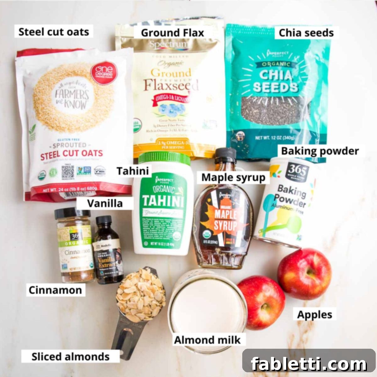 Hearty Baked Steel-Cut Oats 4 Labeled ingredients for baked steel cut oatmeal. Oats, flax, tahini, chia, maple syrup, almond milk, apples, spices.