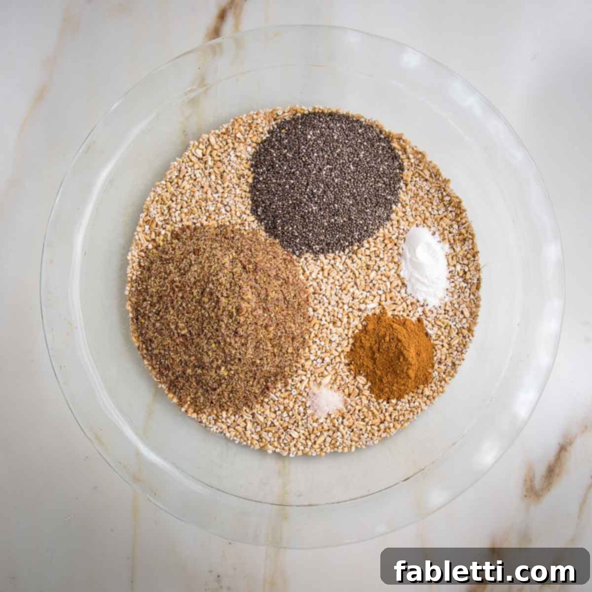 Hearty Baked Steel-Cut Oats 5 Glass pie dish filled with steel cut oats and topped with chia seeds, ground flax, cinnamon and baking powder.