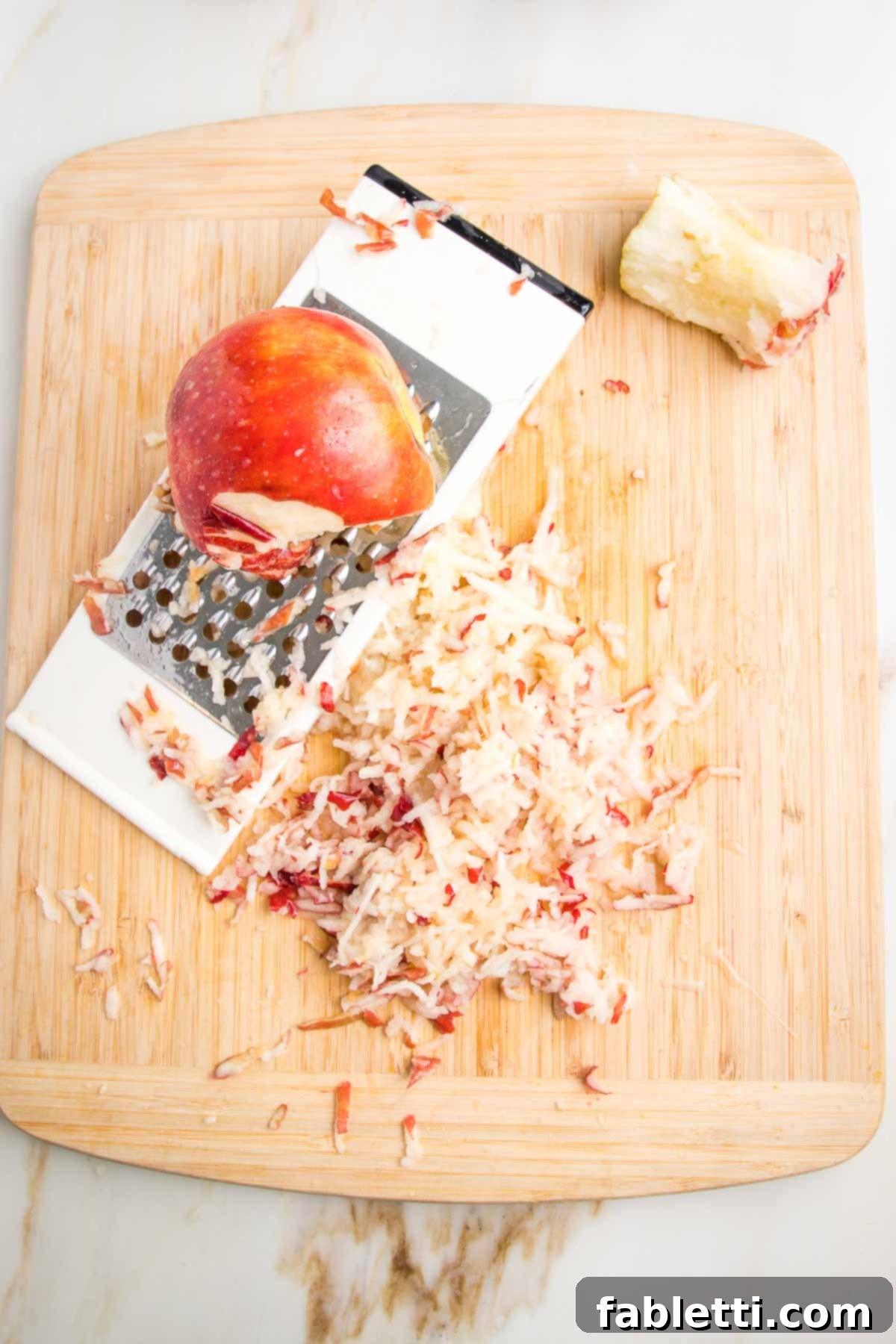 Hearty Baked Steel-Cut Oats 9 Wooden cutting board with side of box grater and two shredded red apples.