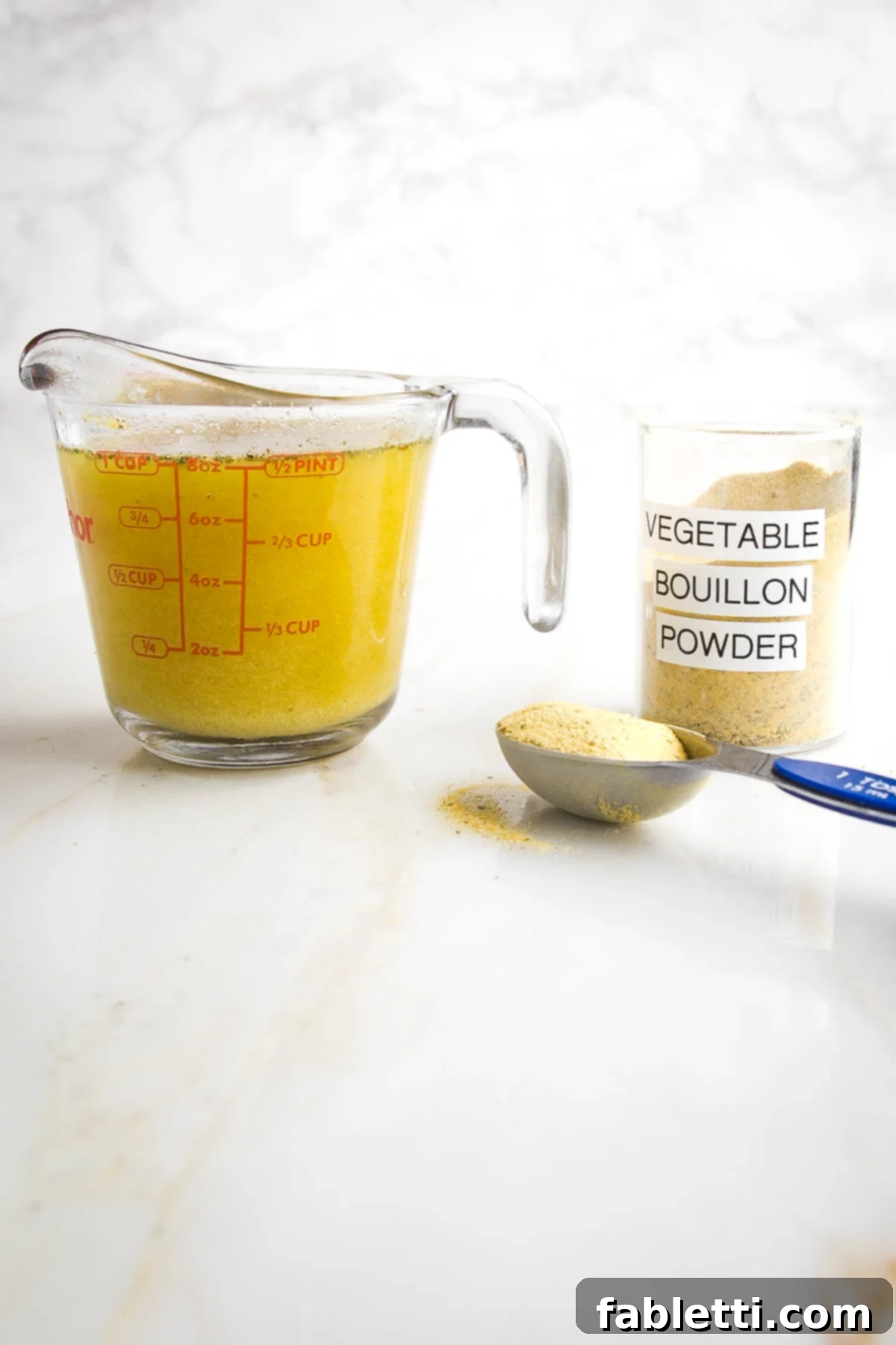 Garden Gold Broth Mix 2 One cup measure of vegetable broth next to a Tablespoon of bouillon powder from a jar marked as such.