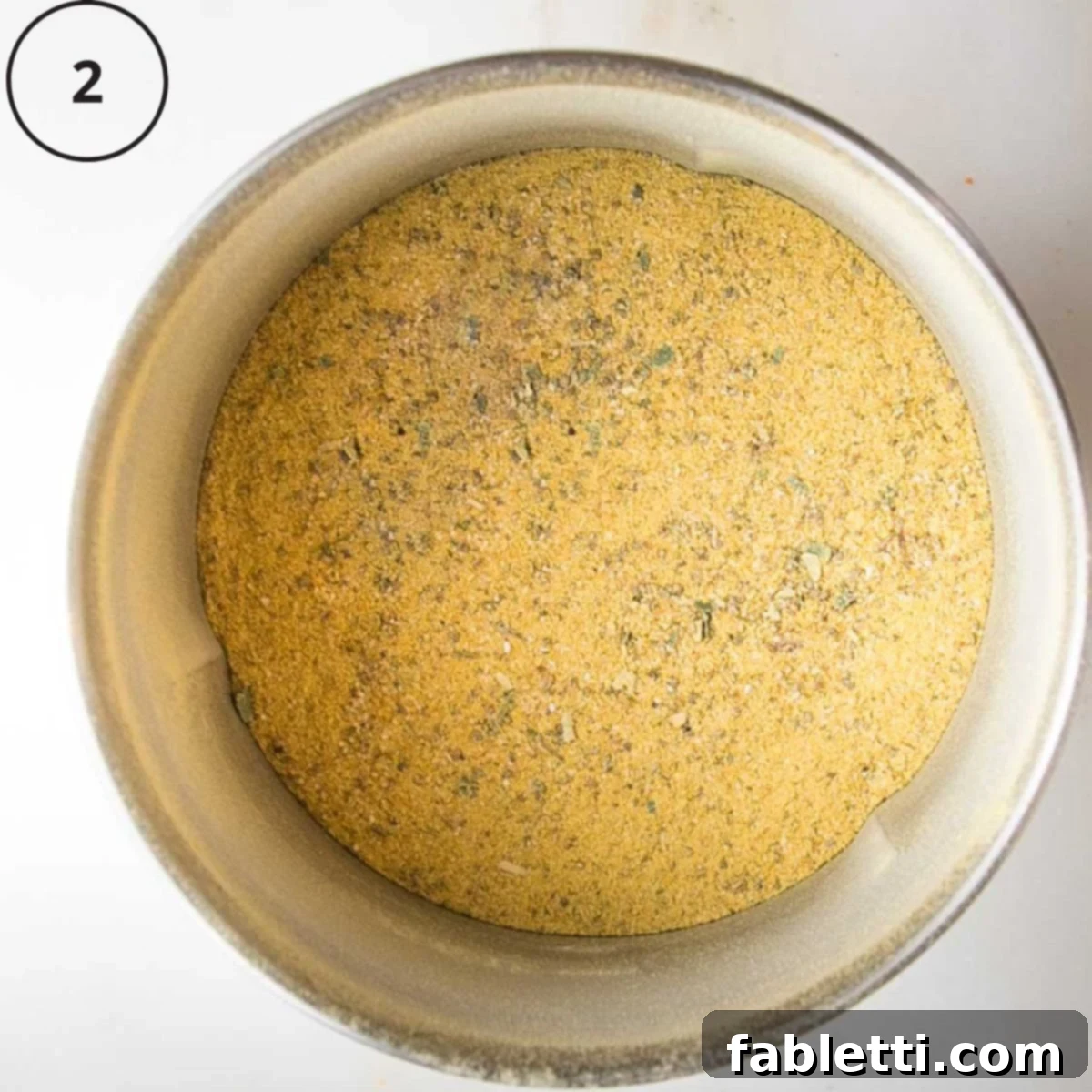 Garden Gold Broth Mix 6 Yellow powder in a spice blender, speckled with green herbs.