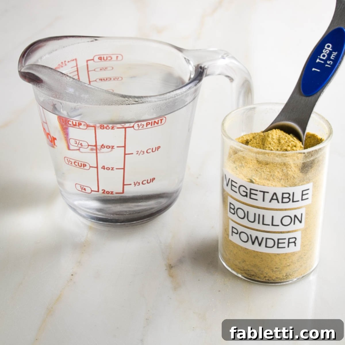 Garden Gold Broth Mix 8 Glass measuring cup with 1 cup water. Spice jar labeled "vegetable bouillon powder" with Tablespoon measuring spoon in it.