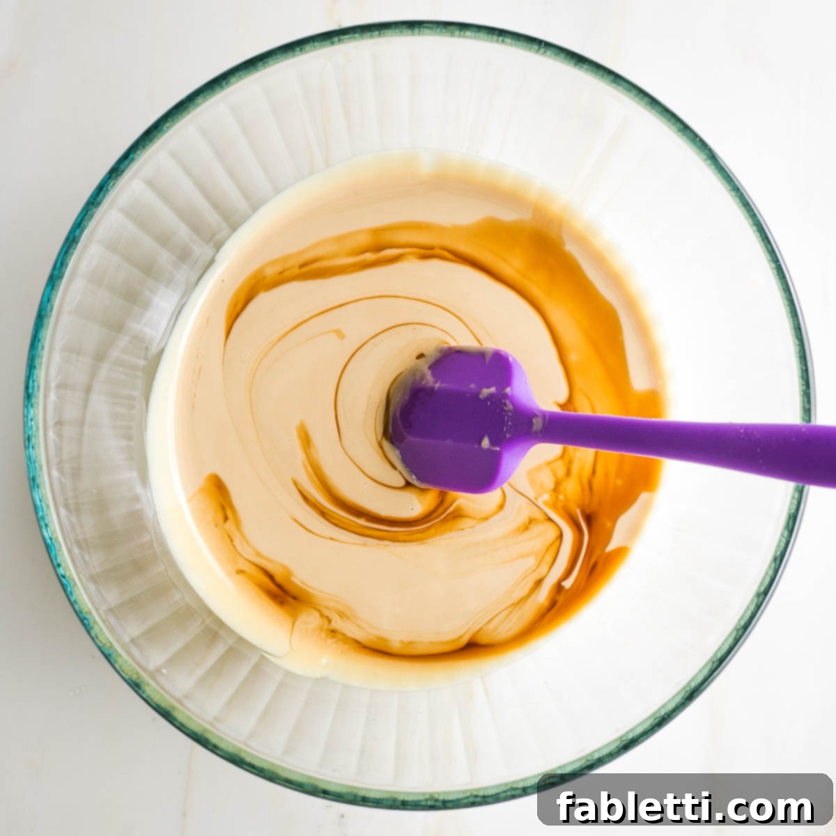 Chewy Vegan Gluten-Free Tahini Chocolate Chip Cookies 5 Tahini, maple syrup and vanilla extract in a large glass bowl with purple spatula.