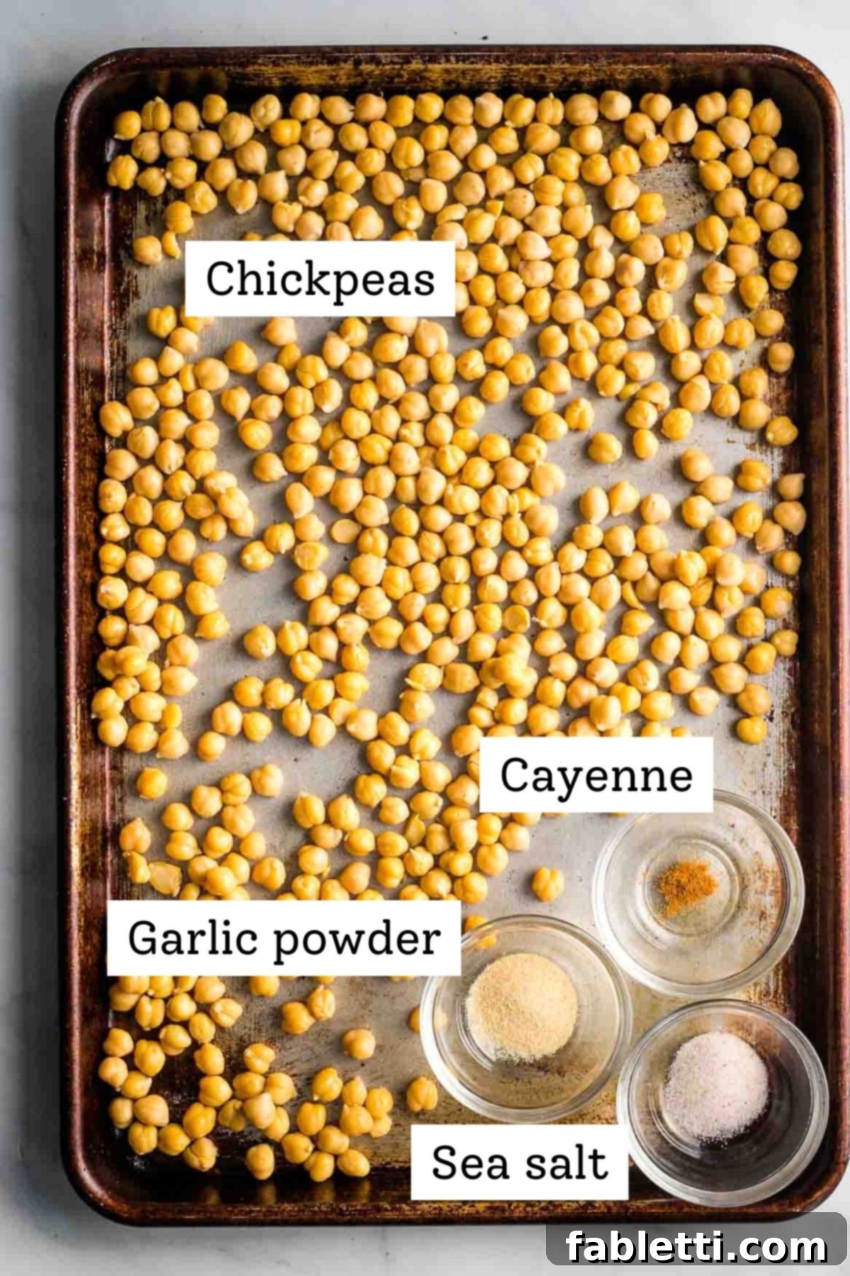 Golden Crispy Chickpea Bites 3 Labeled ingredients on a baking sheet: chickpeas, garlic powder, cayenne, sea salt.