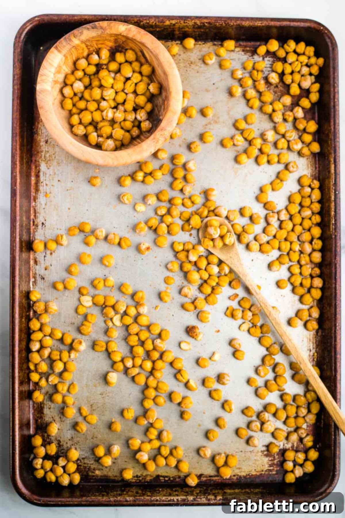 Golden Crispy Chickpea Bites 7 Crunchy chickpeas on a baking tray with a spoon placing them into a bowl.