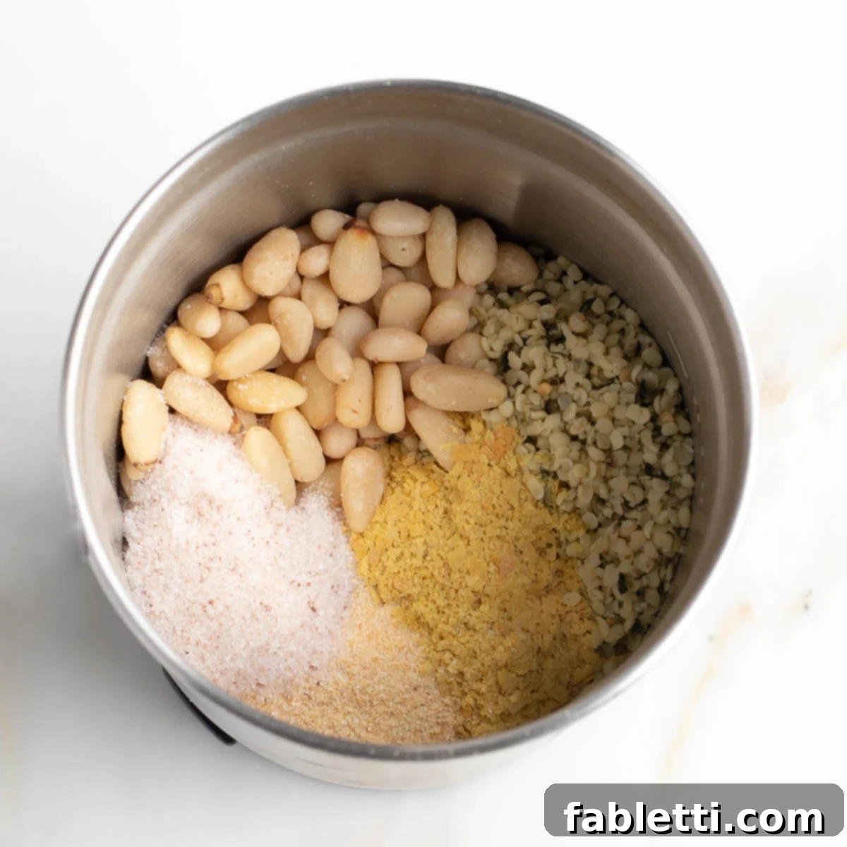 Nut-Free Plant-Based Parmesan 4 Ingredients in the bowl of a spice grinder: pine nuts, hemp seeds, nutritional yeast, garlic powder and salt.