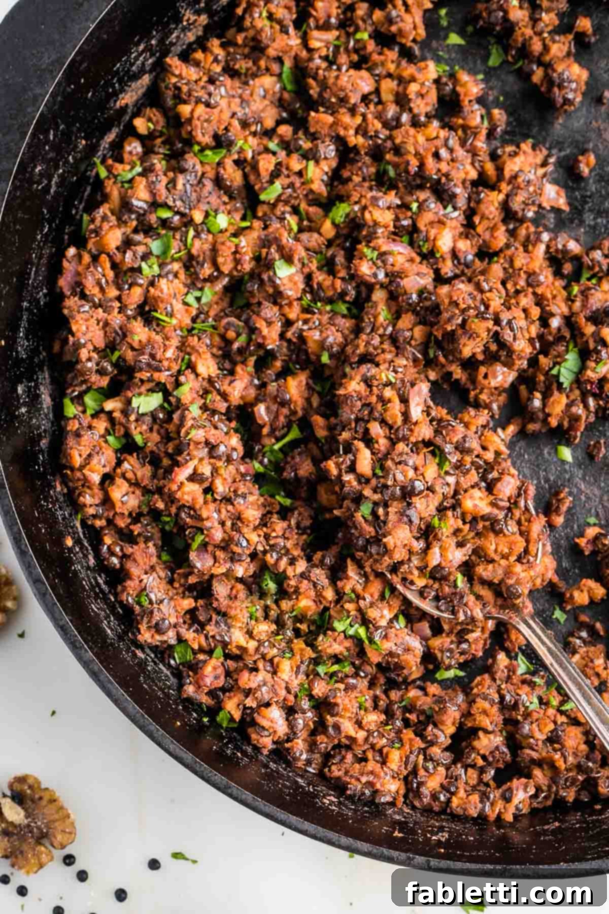 Umami-Packed Vegan Mushroom Lentil Crumble 13 A cast iron skillet holds a vibrant serving of homemade vegan ground beef, beautifully garnished with a sprinkle of fresh chopped parsley, ready to be enjoyed.