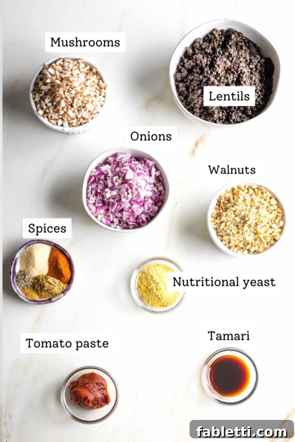 Umami-Packed Vegan Mushroom Lentil Crumble 3 Clearly labeled ingredients for homemade vegan ground beef arranged on a white surface: vibrant beluga lentils, earthy mushrooms, red onions, walnuts, a selection of aromatic spices, nutritional yeast, rich tomato paste, and tamari for umami.