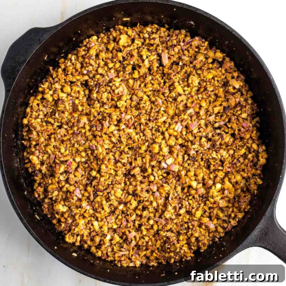 Umami-Packed Vegan Mushroom Lentil Crumble 7 The spice mixture is being thoroughly stirred into the sautéed vegetables and walnuts in the skillet, ensuring even distribution and allowing the aromas to meld, creating a flavorful base.
