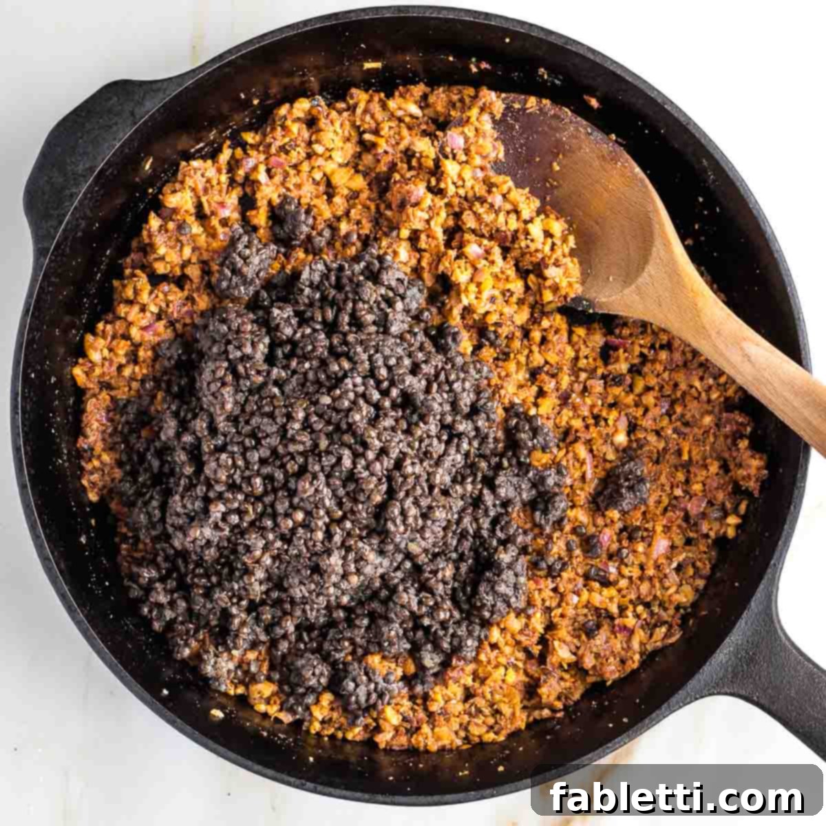 Umami-Packed Vegan Mushroom Lentil Crumble 10 Cooked lentils are being stirred into the fragrant vegetable and spice mixture in the skillet. The components are coming together, promising a rich, textured plant-based ground.