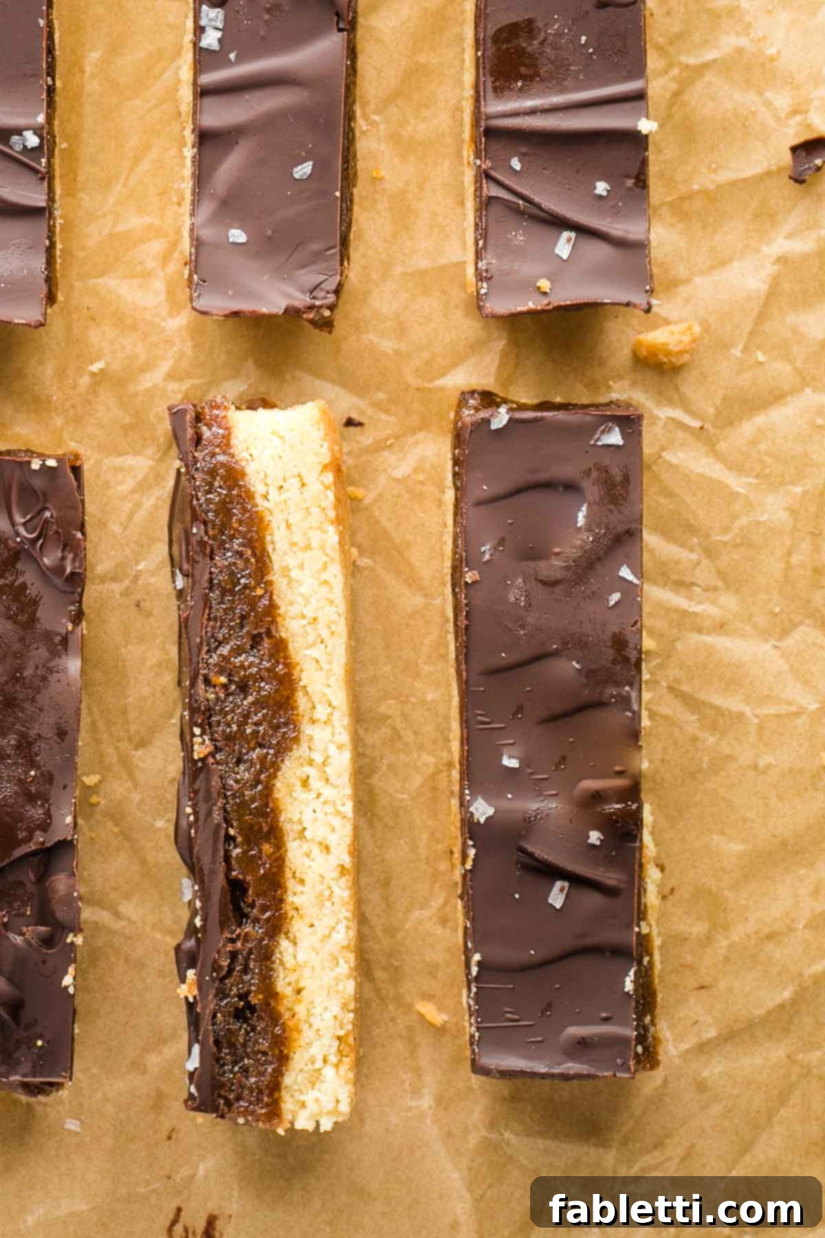 Guilt-Free Homemade Twix Bars 2 Homemade twix bars shown with a sprinkle of flakey sea salt, one turned on its side so you can see the three layers: cookie, caramel, and chocolate.