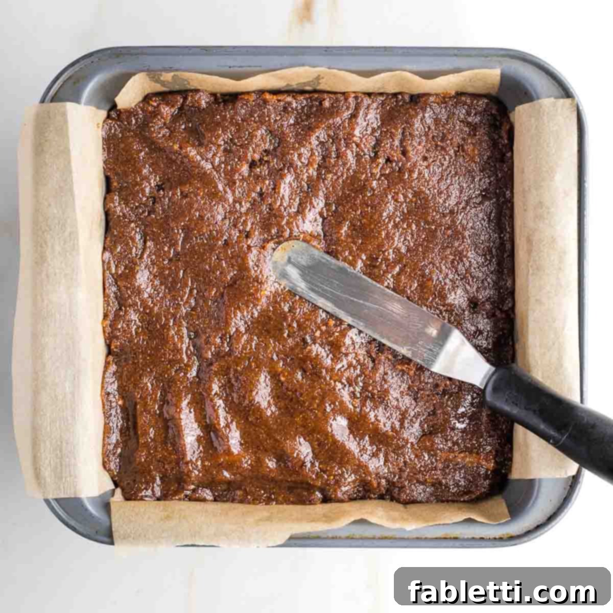 Guilt-Free Homemade Twix Bars 13 An offset spatula smoothly spreading the sticky caramel mixture over the thin, baked biscuit cookie base in the pan.