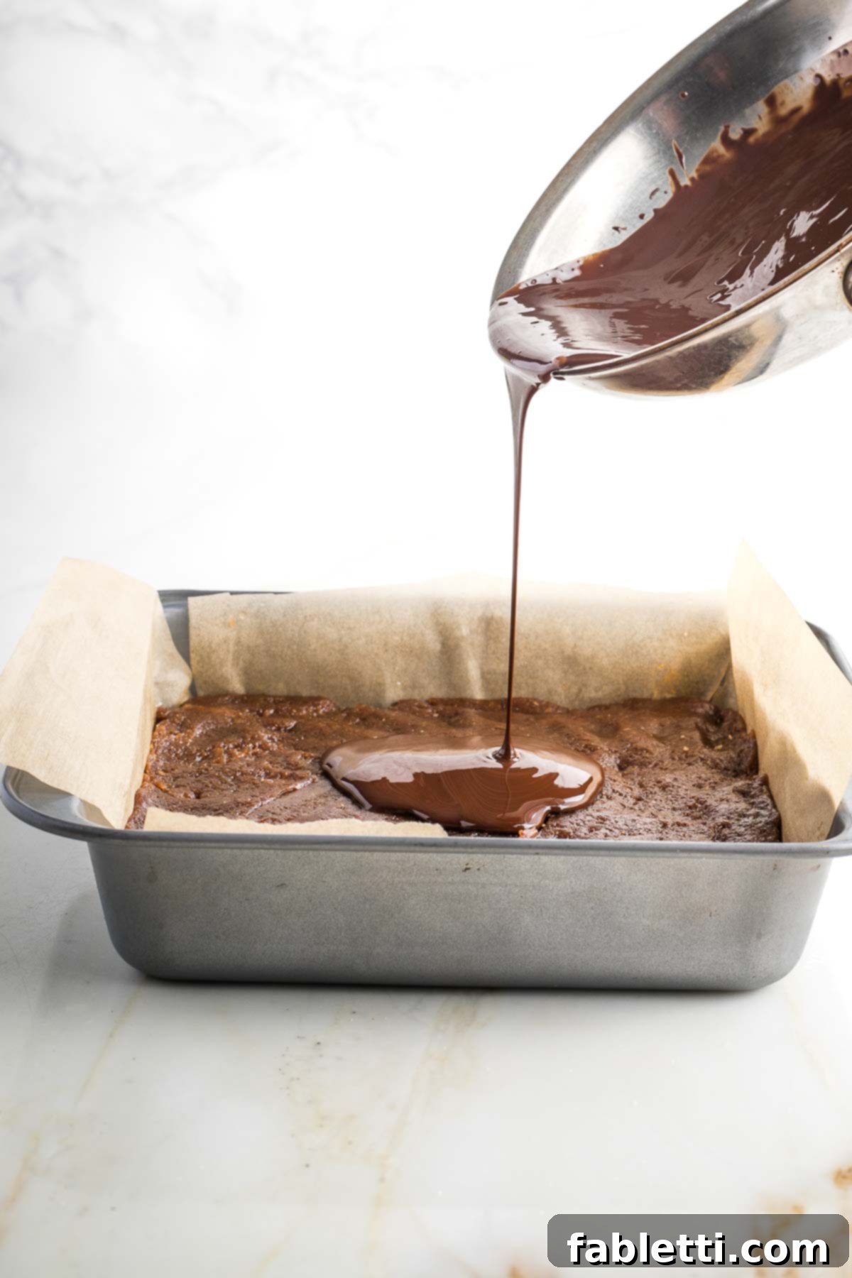 Guilt-Free Homemade Twix Bars 15 Glossy melted chocolate being poured from a small pan over the hardened caramel layer in the square baking pan.