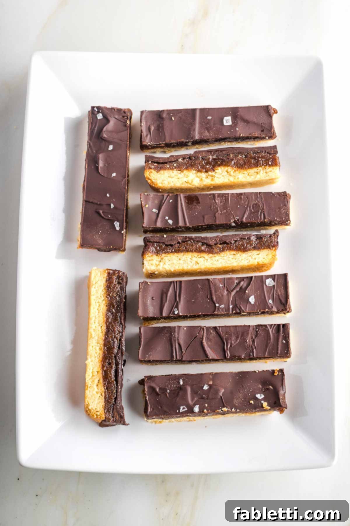 Guilt-Free Homemade Twix Bars 21 Homemade twix bars, some turned sideways to showcase the three distinct layers, artfully arranged on a white platter for serving.