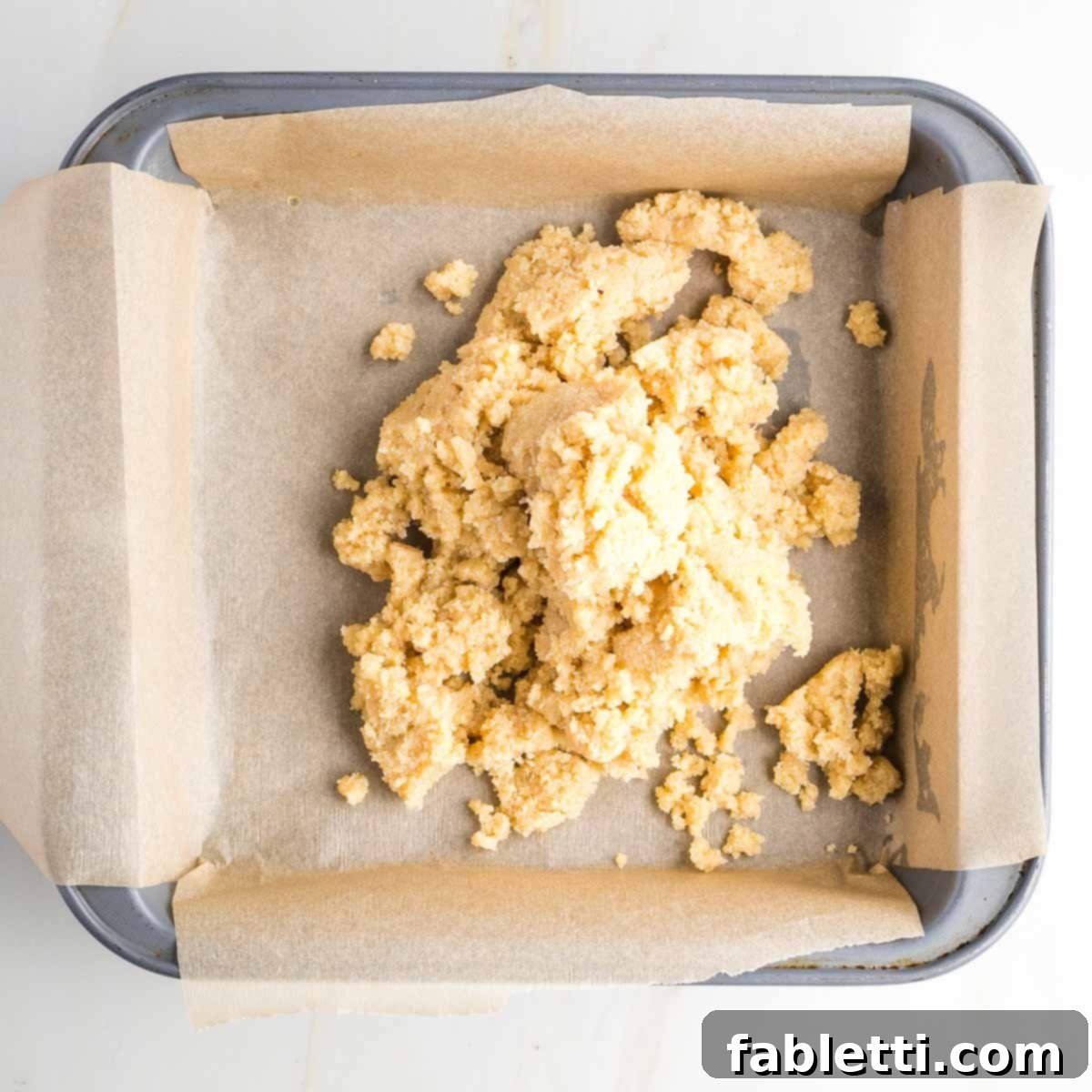 Guilt-Free Homemade Twix Bars 7 Cookie dough gently pressed and evenly distributed into a square pan lined with parchment paper, forming a thin base.