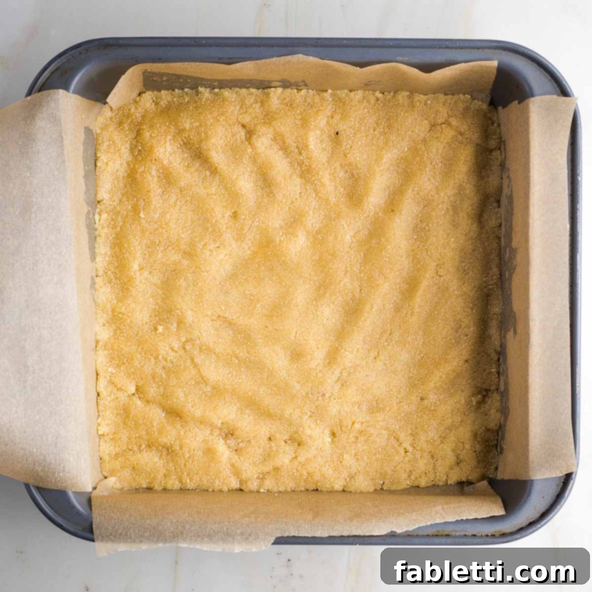 Guilt-Free Homemade Twix Bars 8 Close-up of the cookie dough firmly pressed into the corners of the square baking pan, ready for the oven.