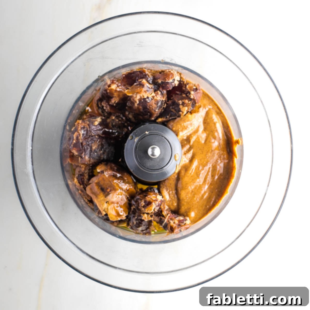 Guilt-Free Homemade Twix Bars 10 Pitted Medjool dates, almond butter, maple syrup, and olive oil in the bowl of a food processor, ready to be blended into caramel.
