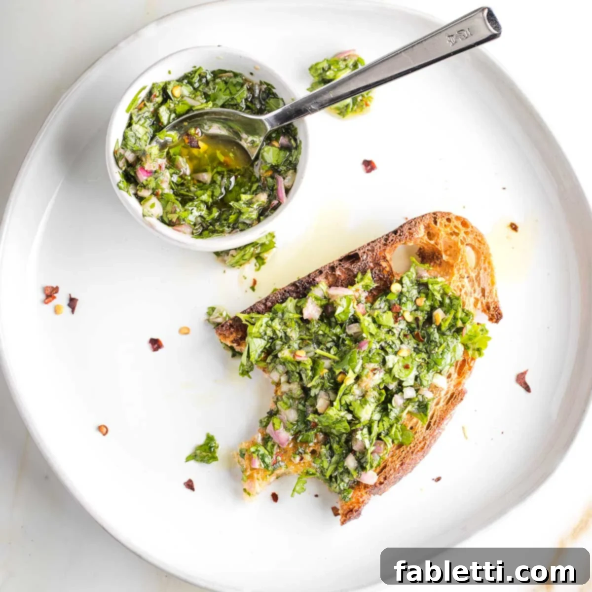 Vibrant Cilantro Chimichurri 11 A piece of sourdough toast with chimichurri and a bite taken, alongside a small dish with more sauce, illustrating a perfect snack or appetizer.