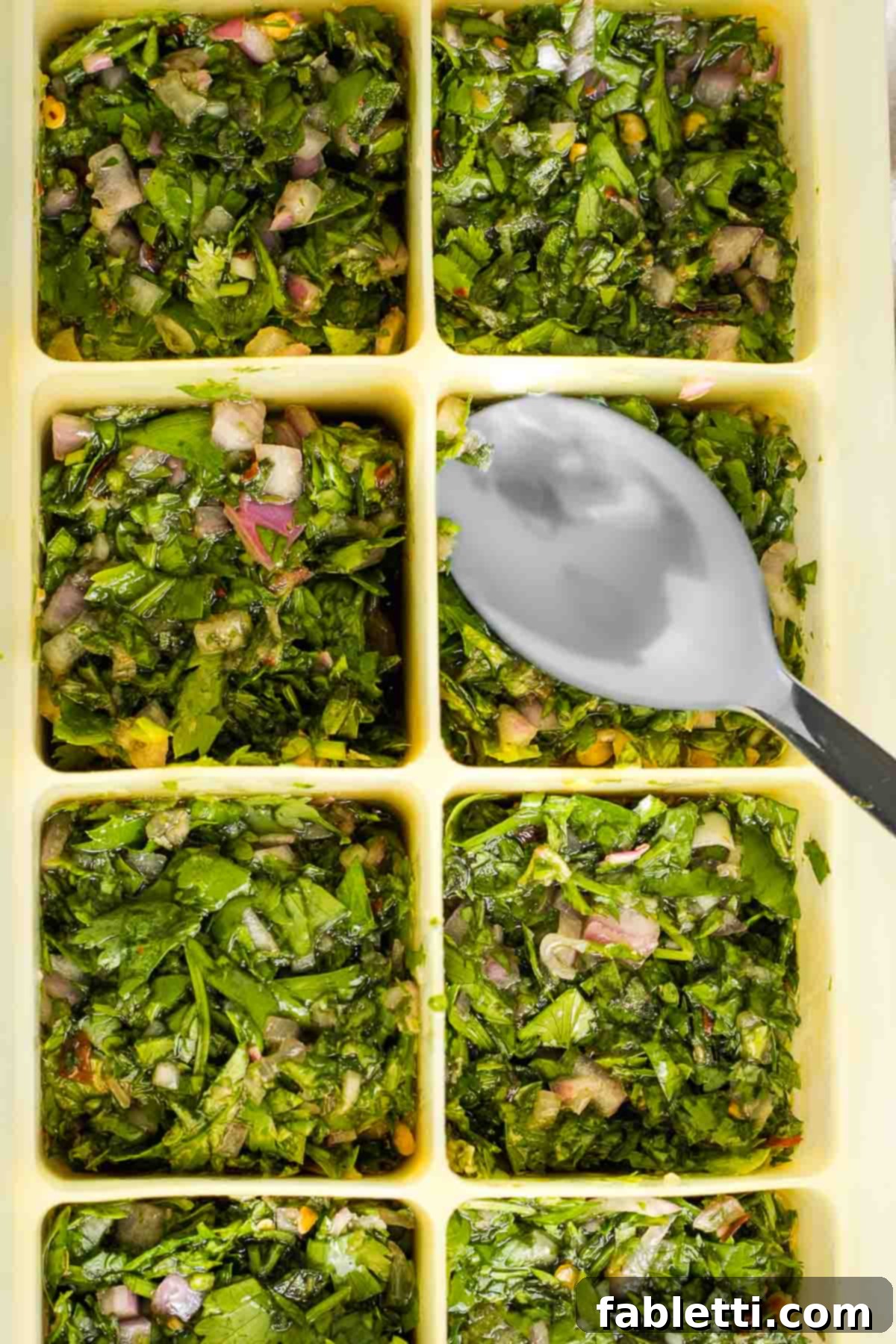 Vibrant Cilantro Chimichurri 12 Chunky, bright green chimichurri sauce packed into an ice cube tray with a spoon, ready for freezing.
