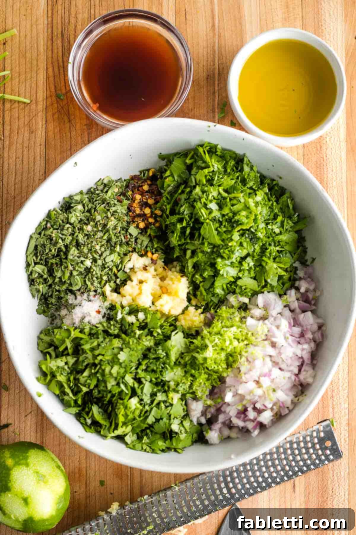 Vibrant Cilantro Chimichurri 7 Bowl with chopped herbs, onion, garlic, salt and pepper, surrounded by small dishes of vinegar, olive oil, and a zested lime.